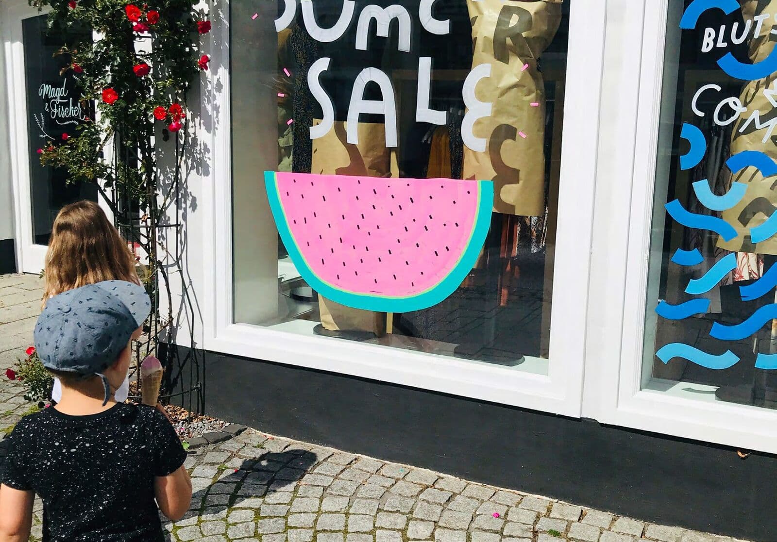 Bemaltes Schaufenster mit „Summer Sale“ und Wassermelone, ein Kind schaut zu