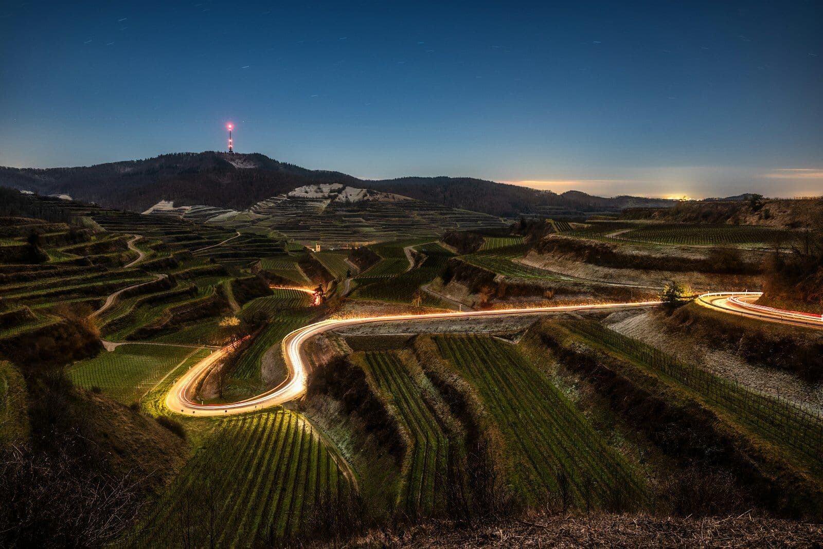 Beleuchtete Straße in Serpentinen durch Weinberge in der Dämmerung