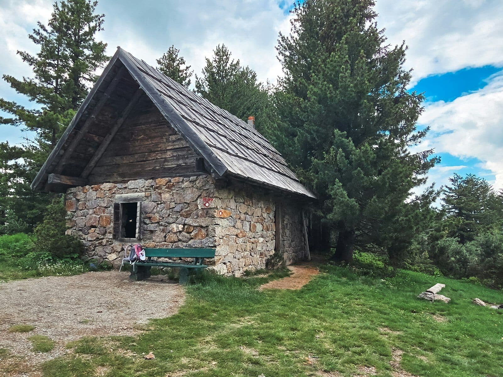 Alte Steinhütte mit Holzdach und Bank unter Tannen
